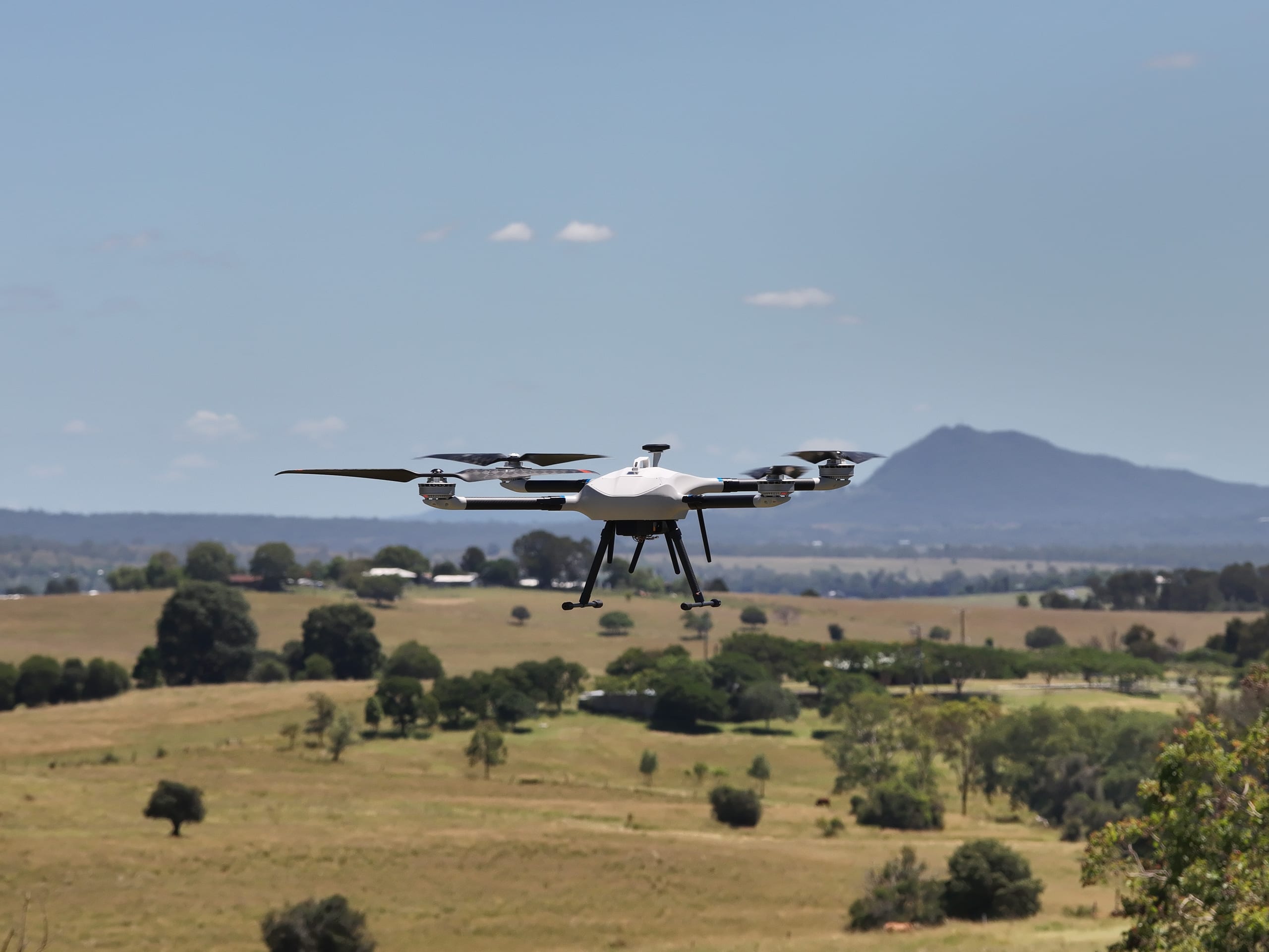 Industrial quadcopter drone in flight over open farmland